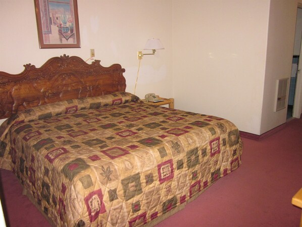Quarto com cabeceira de madeira, colcha acolchoada, mesa de cabeceira com abajur e telefone.