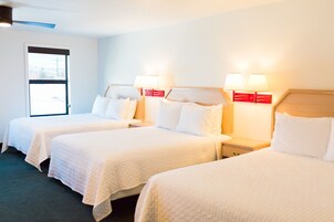 Habitación de hotel con tres camas individuales, cada una con cabecera y mesitas de noche. Se observa una ventana en el lado izquierdo de la habitación.