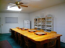 Un comedor con una mesa y sillas de madera, un ventilador de techo, un refrigerador blanco y un aparador de vidrio con vajilla.