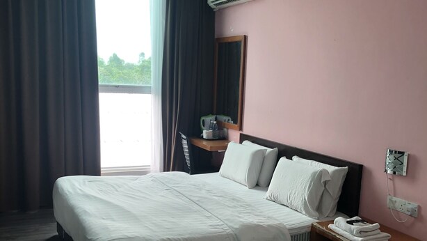 A hotel room with two beds, a desk with a chair, a window with curtains, and an air conditioning unit. - Permai Hotel Sibu (Sibu)