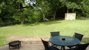 Une terrasse extérieure avec une table ronde et quatre chaises, un foyer et un hamac.