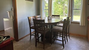 Un coin repas avec une table ronde et six chaises, une fenêtre avec des rideaux et un panneau fixé au mur.