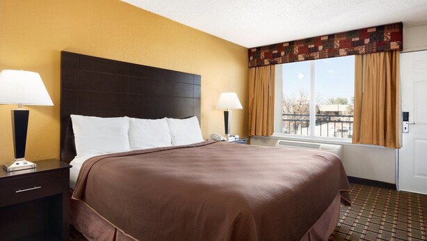 A hotel room with a large bed, two bedside tables with lamps, a window with curtains, and a door. - Super 7 Inn (Midland)