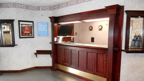A reception area with a wooden counter, a flat-screen TV, and a clock on the wall. - Super 7 Inn (Midland)
