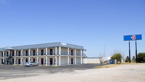 A motel with a two-story structure, a covered parking area, and a clear blue sky. - Super 7 Inn (Midland)