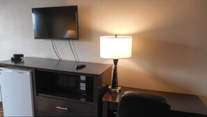 A hotel room with a flat-screen TV mounted on the wall, a desk with a lamp, a microwave, and a chair. - Super 7 Inn (Midland)