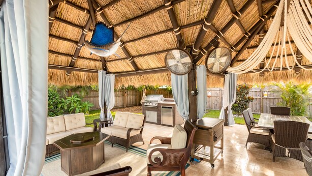 Une terrasse extérieure aménagée avec des meubles en osier, un barbecue et un ventilateur.