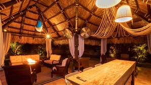 Un espace extérieur aménagé avec des sièges, un toit de chaume, des meubles en osier et une table en bois.