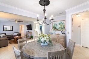 Un comedor con una mesa de madera, sillas, una araña y un centro de mesa floral.