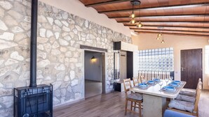 Un comedor con pared de piedra, vigas de madera en el techo y una mesa dispuesta para seis personas, con platos y vasos azules.