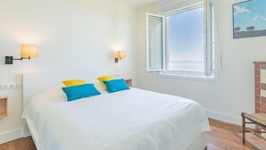 Ein Hotelzimmer mit einem großen Bett, zwei Wandlampen, einem Fenster mit geöffnetem Rollo und einem Gemälde an der Wand.