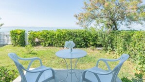 Eine Terrasse mit einem runden Tisch und zwei Stühlen, umgeben von Grünpflanzen und Meerblick.