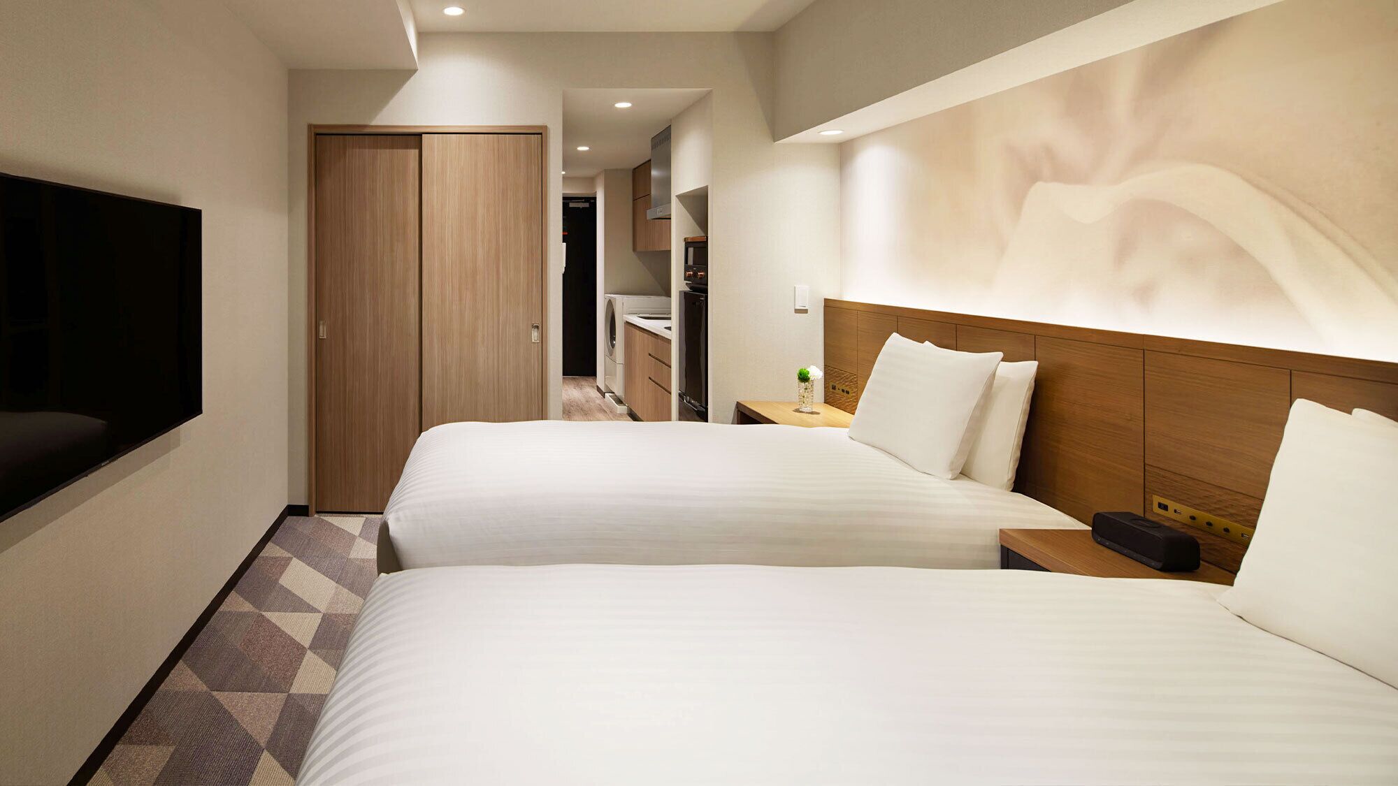 Habitación de hotel con dos camas, un televisor, un armario de madera y un baño visible al fondo.