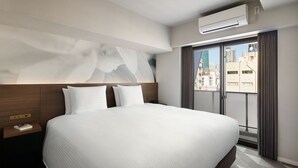 Hotelkamer met een groot bed, nachtkastje, een wandairconditioner en uitzicht op de stad door een raam.
