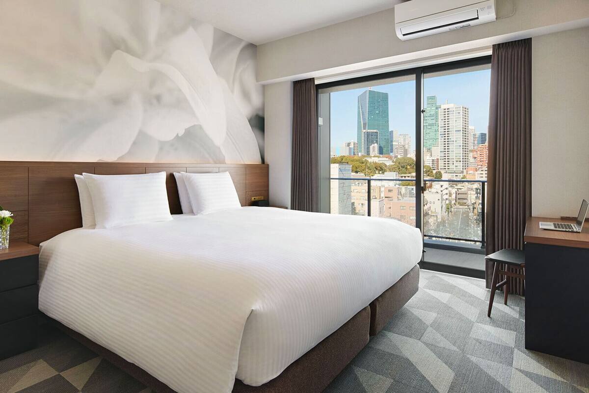 A modern hotel room with a large bed, a desk, and a view of a cityscape.