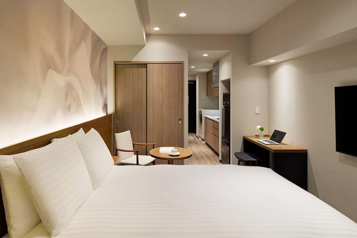 A hotel room with a large bed, a desk with a laptop, a chair, and a TV.