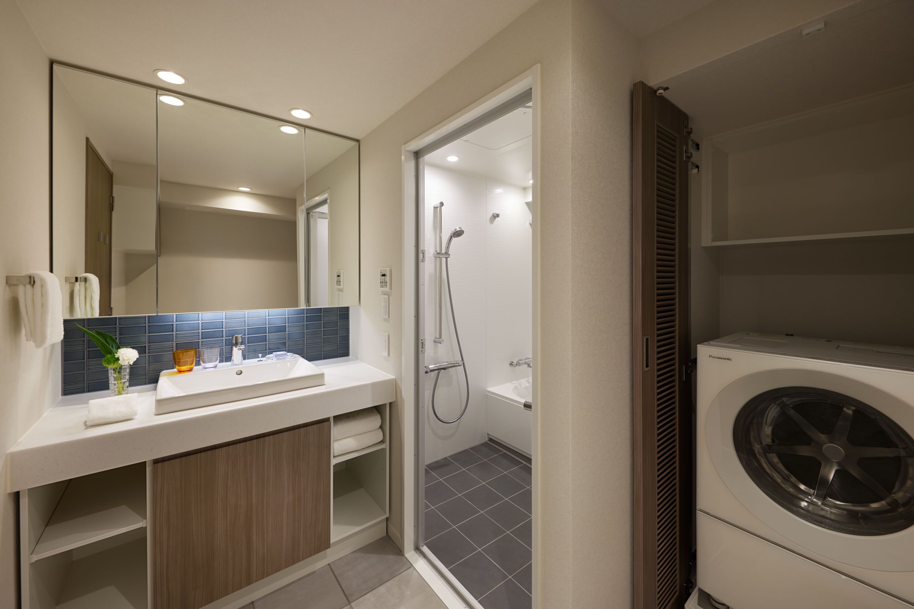 A modern bathroom with a large mirror, a sink, a shower, and a built-in washing machine.