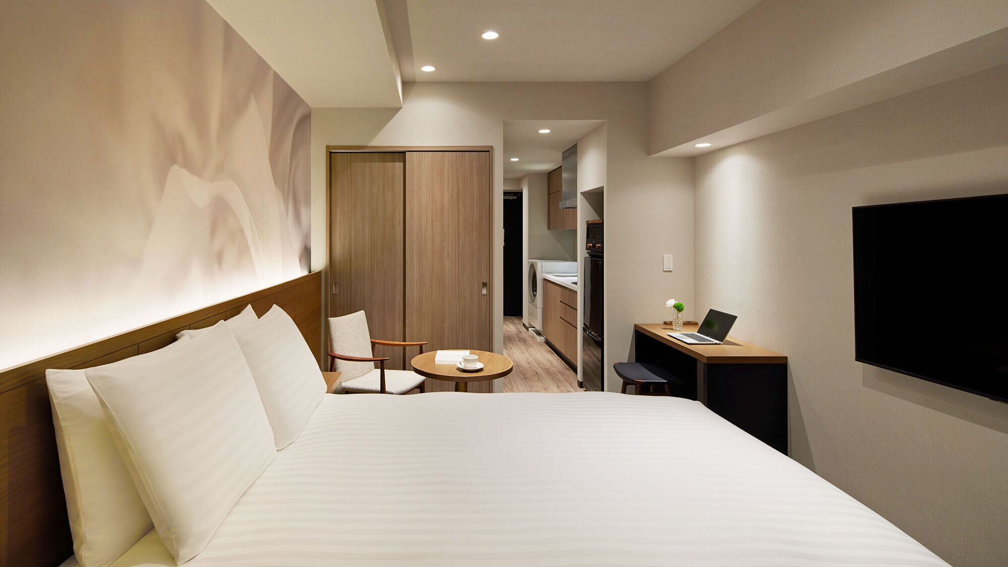Habitación de hotel con una cama grande, un escritorio con una computadora portátil, un televisor y una pequeña mesa de comedor.