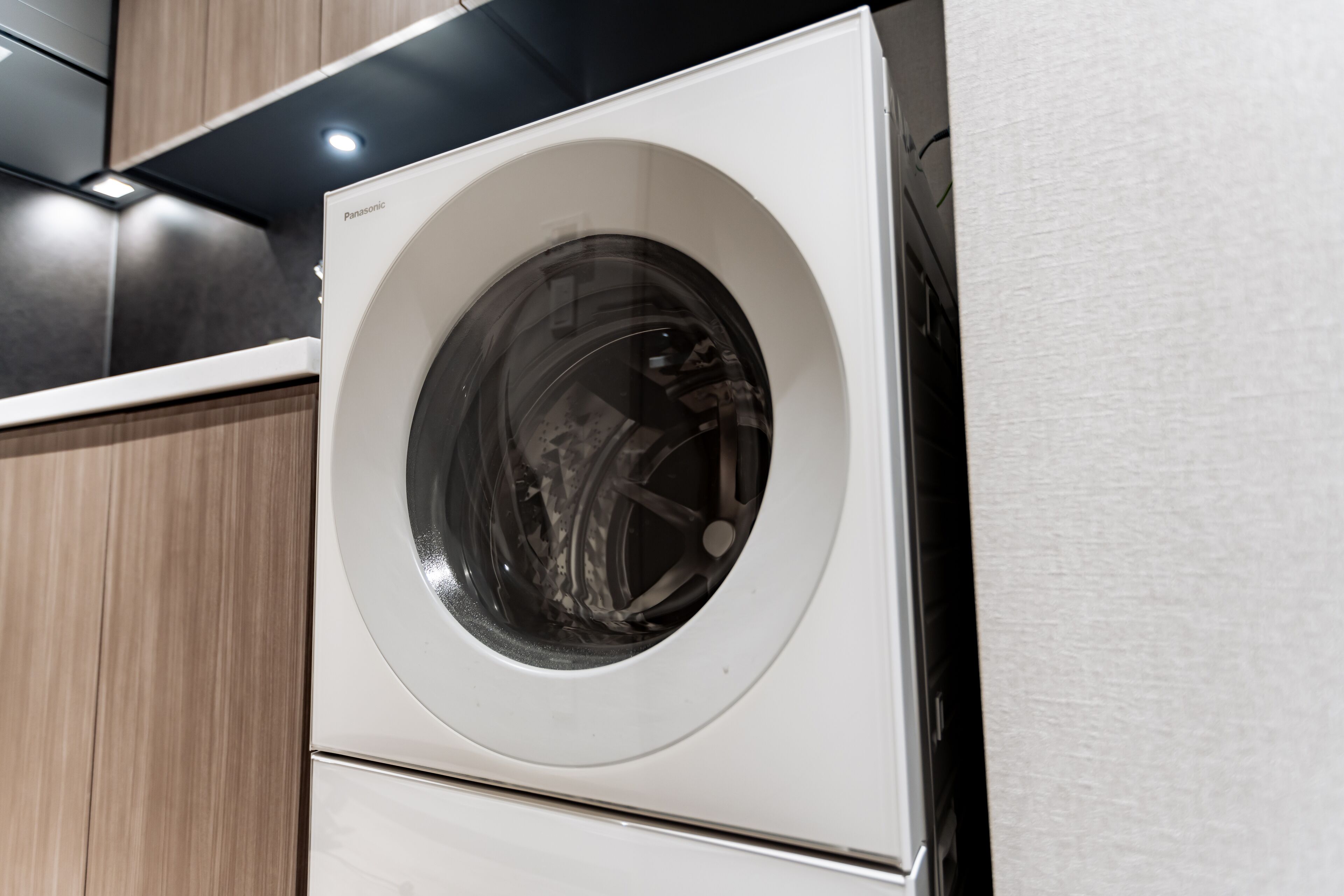 A front view of a white washing machine with a Panasonic logo, set against a wooden cabinet backdrop.