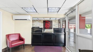 A reception area with a red leather chair, a reception desk, a Red Roof Inn sign, and a view through large windows. - Red Roof Inn Berea (Berea)