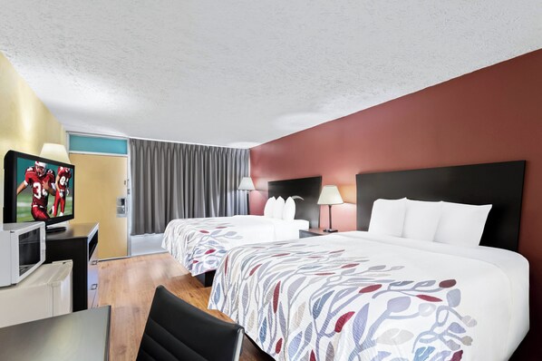 Ein Hotelzimmer mit zwei Betten, einem Fernseher, einem Schreibtisch und einem Sessel.