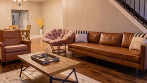 A living room with a brown leather sofa, a wooden coffee table, a brown leather armchair, and a round, fluffy chair.