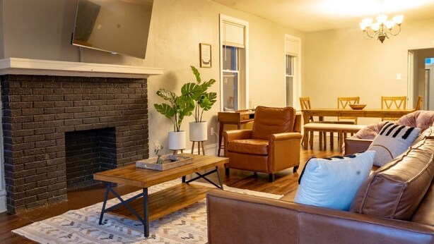 A living room with a brick fireplace, leather sofa, wooden coffee table, and a dining area with a table and chairs.