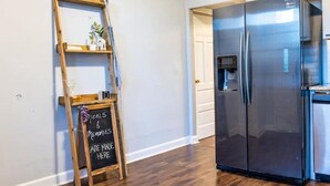 A kitchen with a stainless steel refrigerator, a wooden ladder shelf with decorative items, and a chalkboard sign.