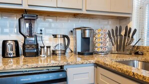 A kitchen with a granite countertop, a coffee maker, a blender, a toaster, a coffee pot, a knife block, and a dishwasher.