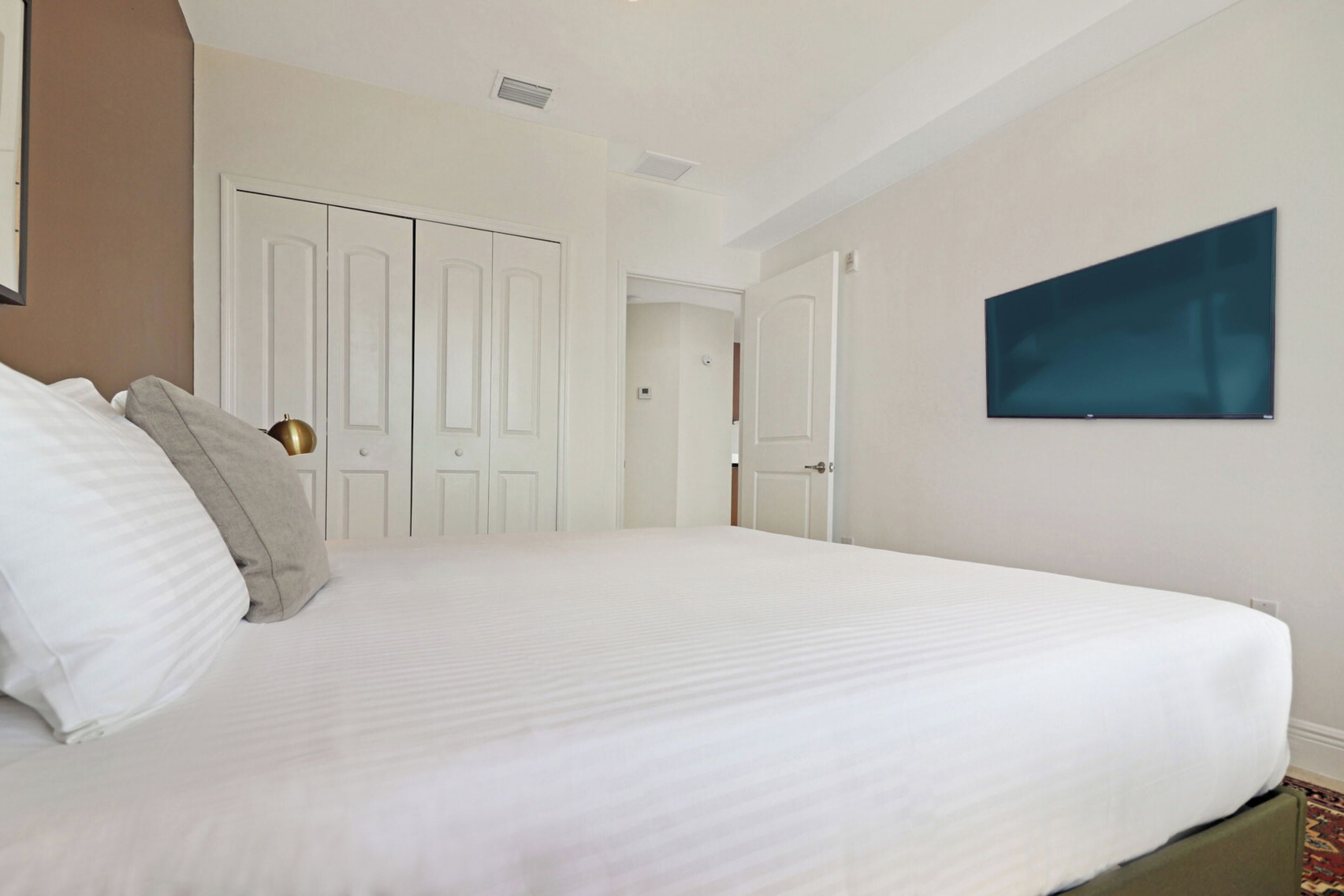 A hotel room with a large bed, white walls, a mounted TV, and a door leading to another room.