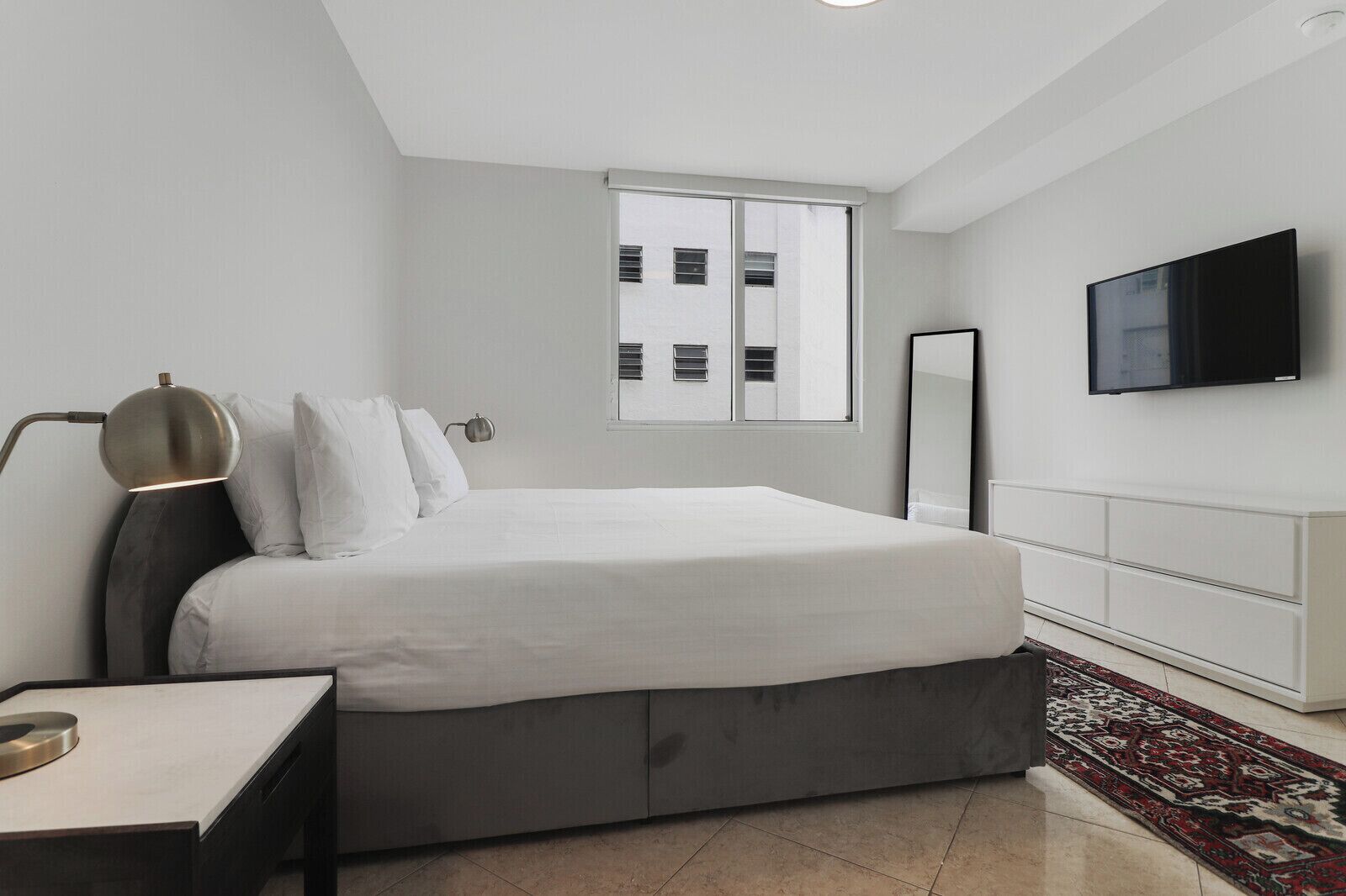 Una camera da letto moderna con un letto grande, un comodino, una lampada, un televisore e una finestra con tende.
