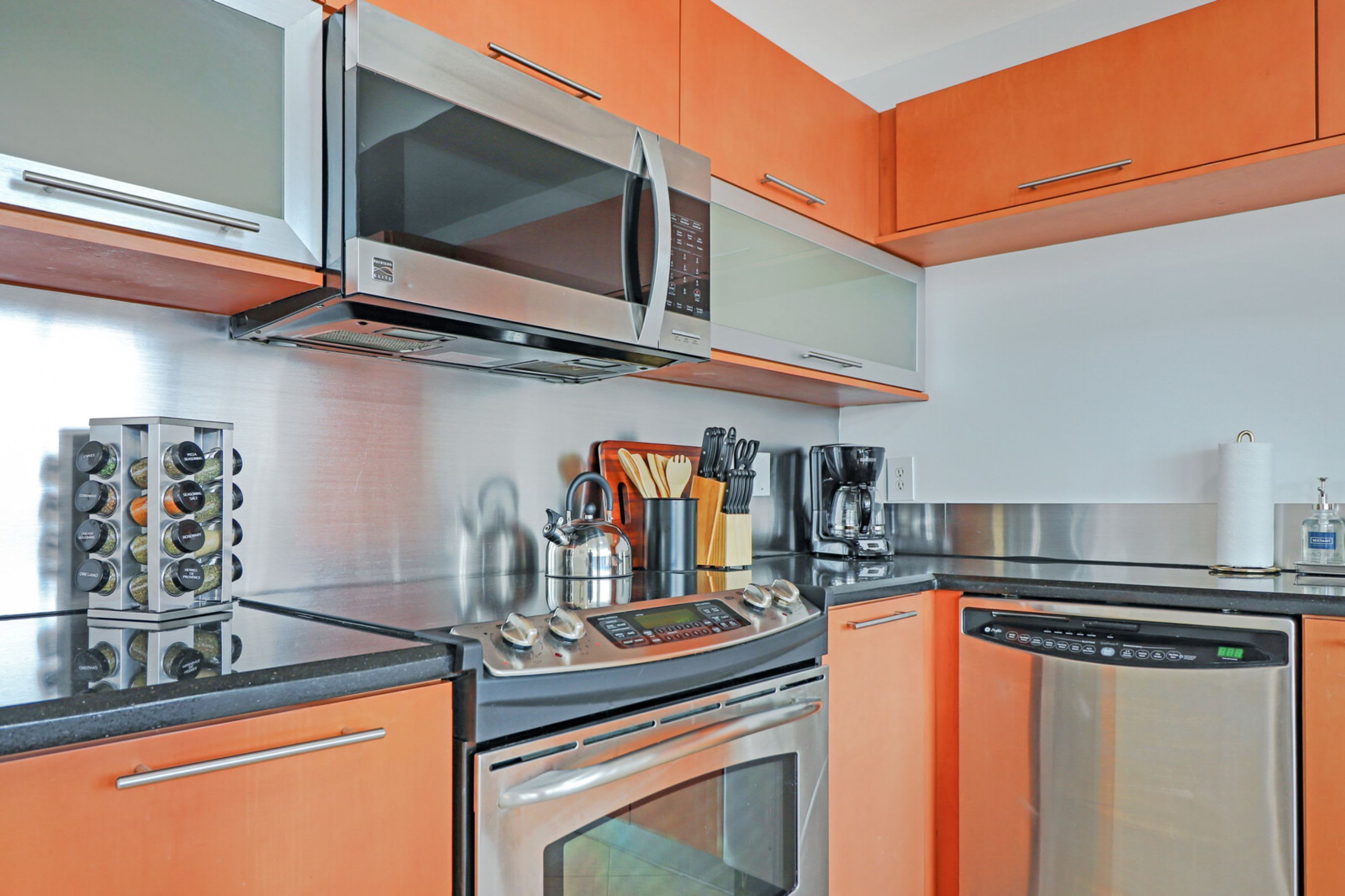 A kitchen with stainless steel appliances, including a microwave, oven, and dishwasher, and orange cabinetry.
