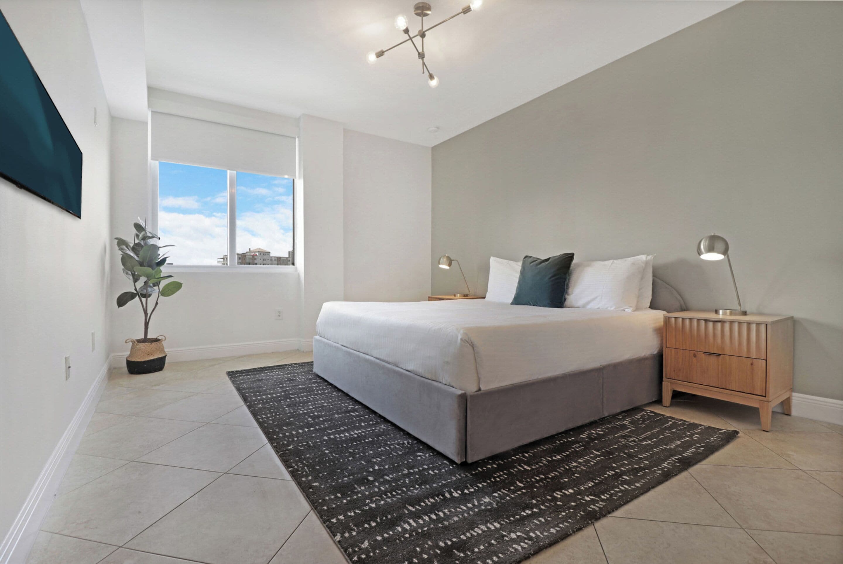 Une chambre moderne avec un grand lit, une table de chevet, une lampe, une plante en pot et une vue sur le ciel par la fenêtre.