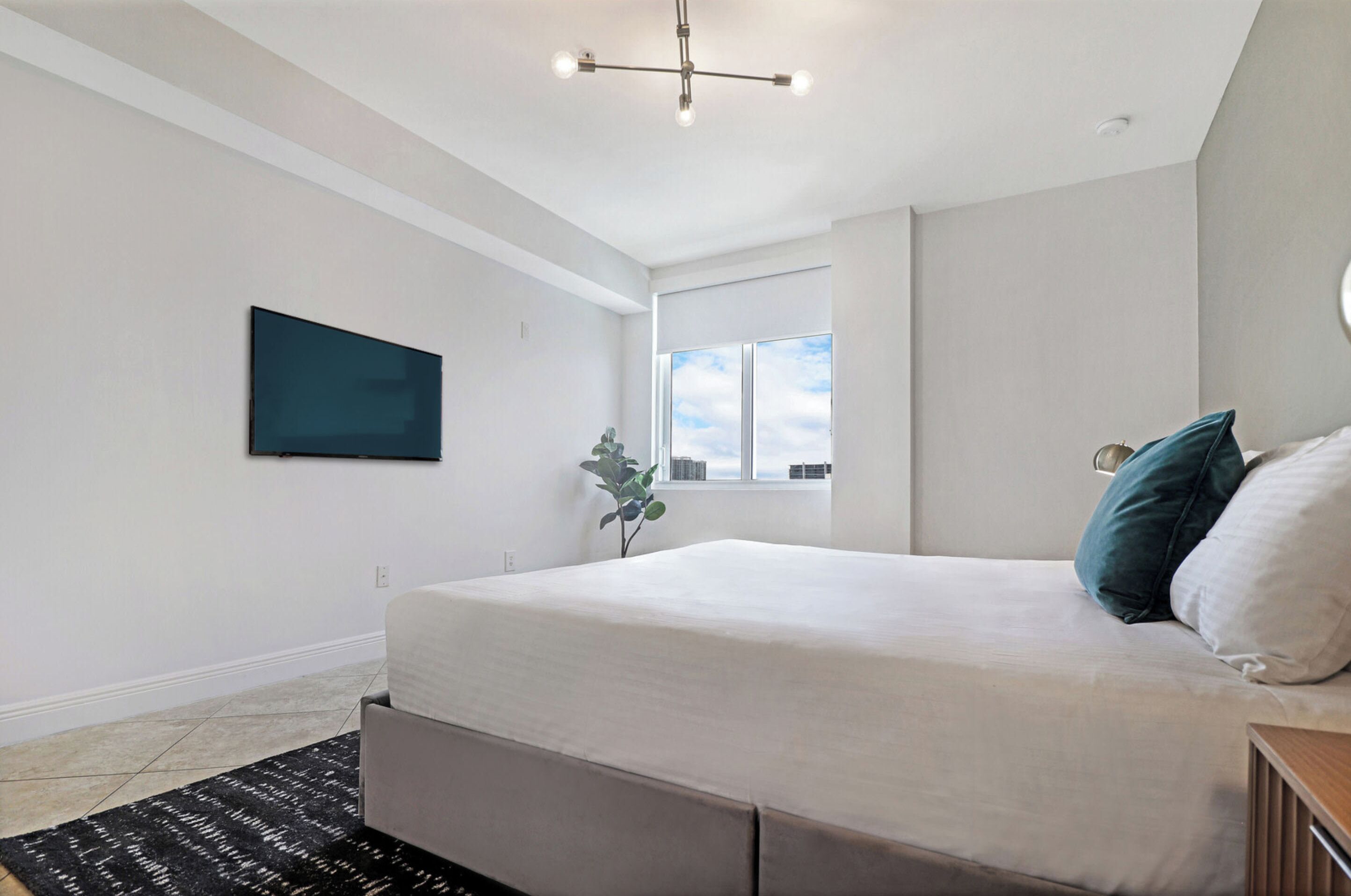 Une chambre moderne avec un lit, un téléviseur fixé au mur, une fenêtre donnant sur un beau paysage et un luminaire au plafond.
