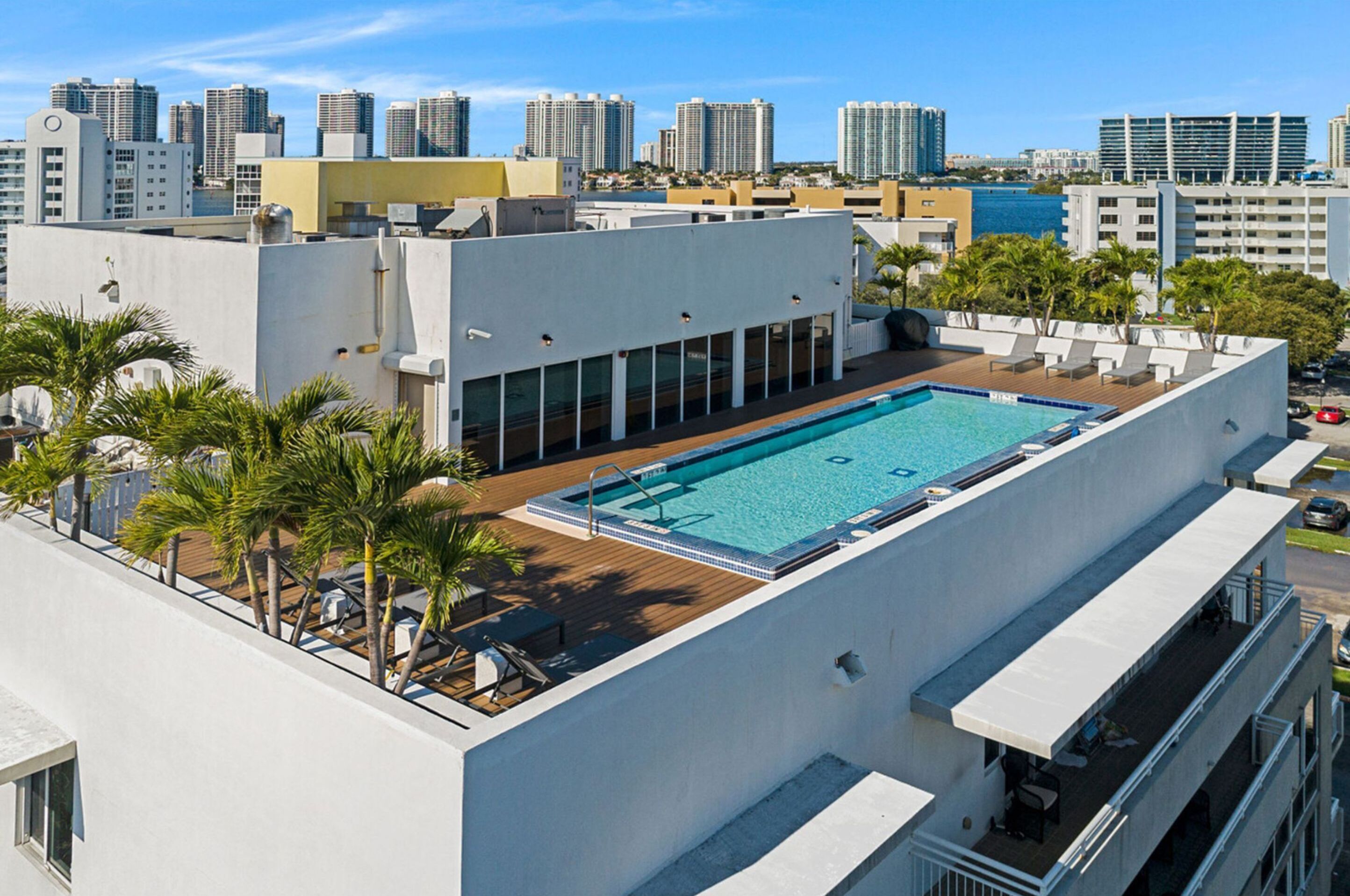 A rooftop pool with a view of the city skyline, surrounded by palm trees and lounge chairs.