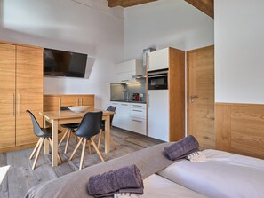 Una camera moderna con un tavolo da pranzo in legno, sedie nere, un letto con coperta grigia e un angolo cottura con forno a microonde e forno.