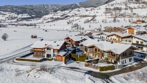 A snow-covered mountain village with modern wooden houses, a ski slope, and a clear blue sky.