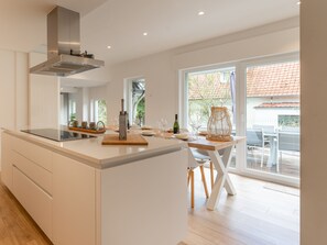 A modern kitchen with a central island, a built-in stove, and a large window providing natural light. - Beautiful holiday home near the beach (Koksijde)