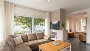 Ein modernes Wohnzimmer mit einem Ecksofa, einem Holztisch, einem Flachbildfernseher und einem Essbereich mit einer Treppe.