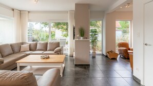 Ein modernes Wohnzimmer mit einem beigen Sofa, einem Holztisch und einem großen Fenster mit Blick ins Freie.