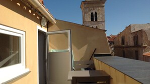 Eine Dachterrasse mit Tisch und Stühlen, eine teilweise geöffnete Tür und im Hintergrund der Blick auf einen historischen Turm.