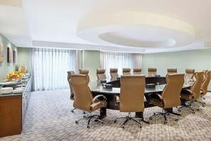 Ein Konferenzraum mit einem großen, ovalen Tisch, beigefarbenen Stühlen und einem Buffetbereich mit Früchten und Getränken.