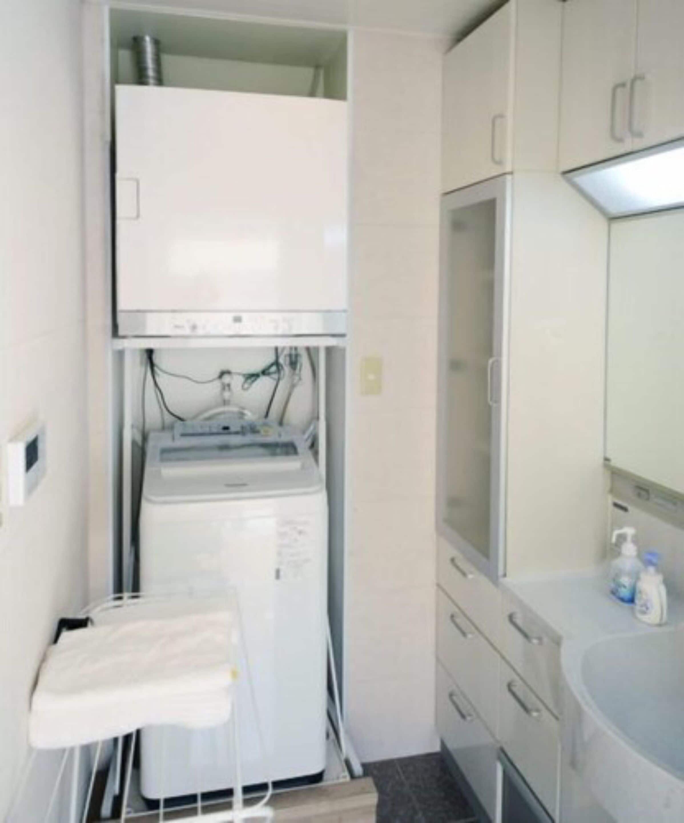 Une salle de bain compacte équipée d’un lave-linge et d’un sèche-linge intégrés, d’une petite table et d’un lavabo avec des articles de toilette.