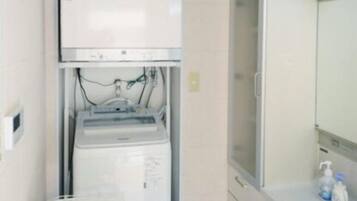 A compact bathroom with a built-in washer and dryer, a small table, and a sink with toiletries.