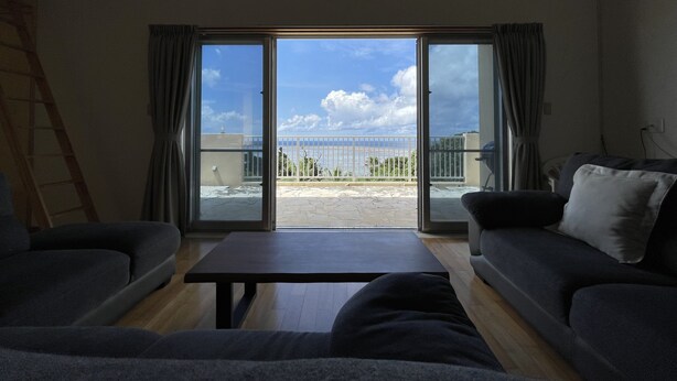 Ein Wohnzimmer mit einer großen Schiebeglaswand, die auf einen Balkon mit Blick auf eine Brücke und einen Strand führt.