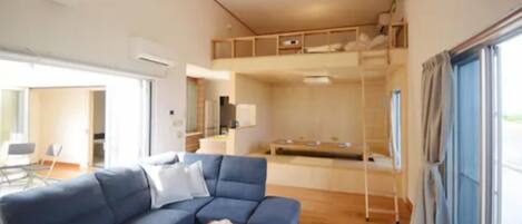 A modern living room with a blue sofa, a wooden coffee table, and a bunk bed in the background.