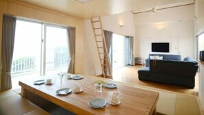 Ein modernes Wohnzimmer mit einem Holzes Esstisch, gedecktem für vier Personen, einem dunklen Sofa und einem an der Wand montierten Fernseher.