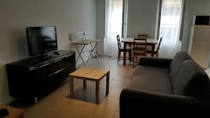 Ett vardagsrum med en TV, en soffa, ett litet bord och en matplats med stolar och ett bord.