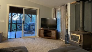 A living room with a television, a fireplace, and a sliding glass door leading to an outdoor area. - Cabin in the Pines - 3 Minutes to the beach, docks or golf! (Cascade)