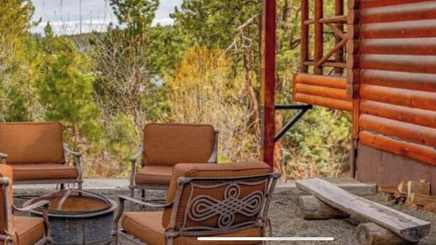 A rustic outdoor seating area with wooden chairs and a metal table, surrounded by a wooden fence and dense foliage. - Cabin in the Pines - 3 Minutes to the beach, docks or golf! (Cascade)